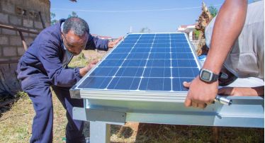 Two persons install a solar dryer for seeds outside a building.