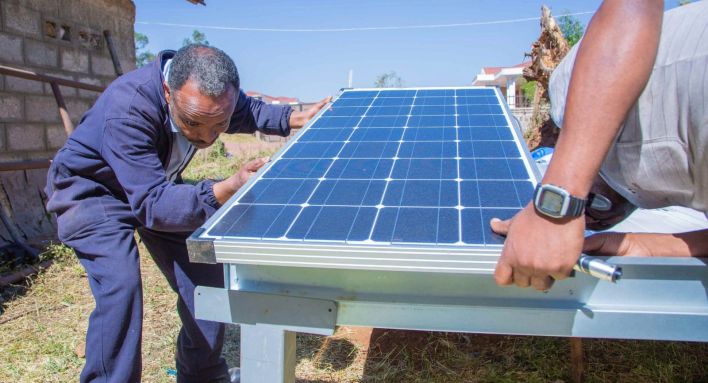 Two persons install a solar dryer for seeds outside a building.