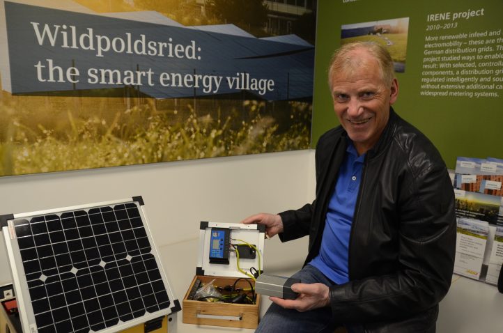 Günter Mögele, Deputy Mayor of Wildpoldsried, Bavaria, with a solar kit in front of a poster reading "Wildpoldsried: the smart energy village".