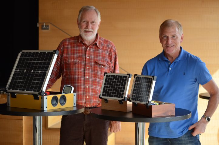 Two people show one large and two small photovoltaic kits in suitcases at bar tables.